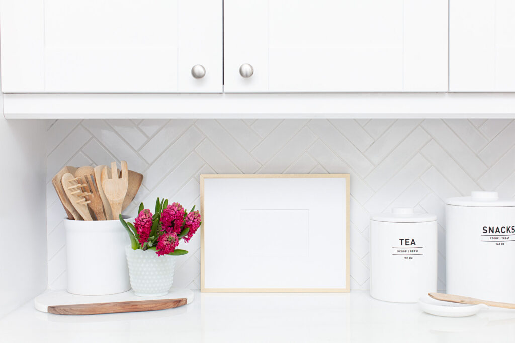Image of kitchen counter with picture frame and tea and snack canisters on the right and cooking utensils and flowers on the left.
