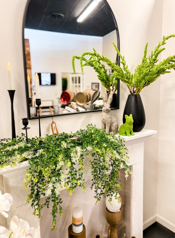 image of mantle decorated for spring with greenery, candlesticks, bunnies and a vase with green stems