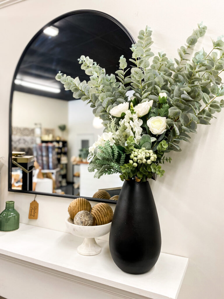 picture of a mantel with a black vase full of flowers and stems
