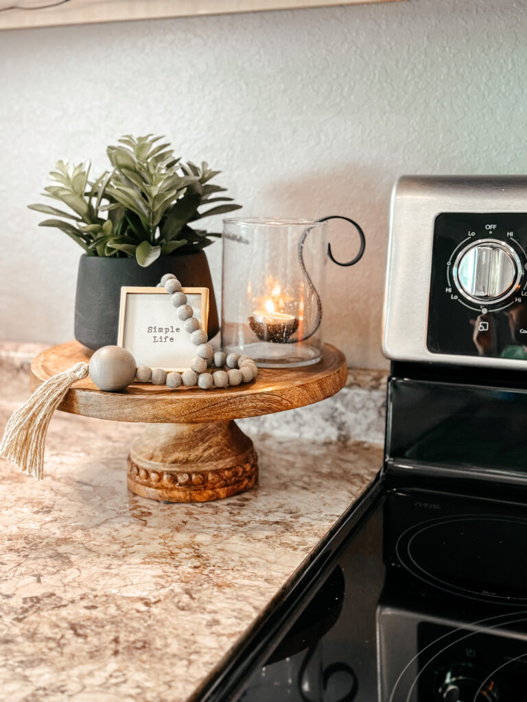 kitchen counter with a wood stand with a potted plant, small sign, beads and votive with tealight candle